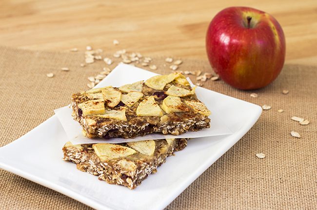 Apple pie healthy oatmeal bars cut and laying on a white plate that is sitting on a wooden surface with an apple in the background