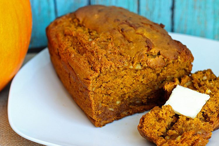 Loaf of pumpkin bread on a white plate with blue background