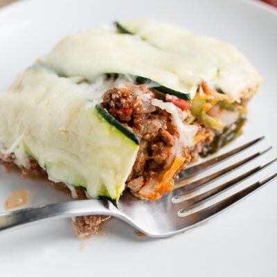 Up close picture of a slice of zucchini lasagna on a white plate with a fork