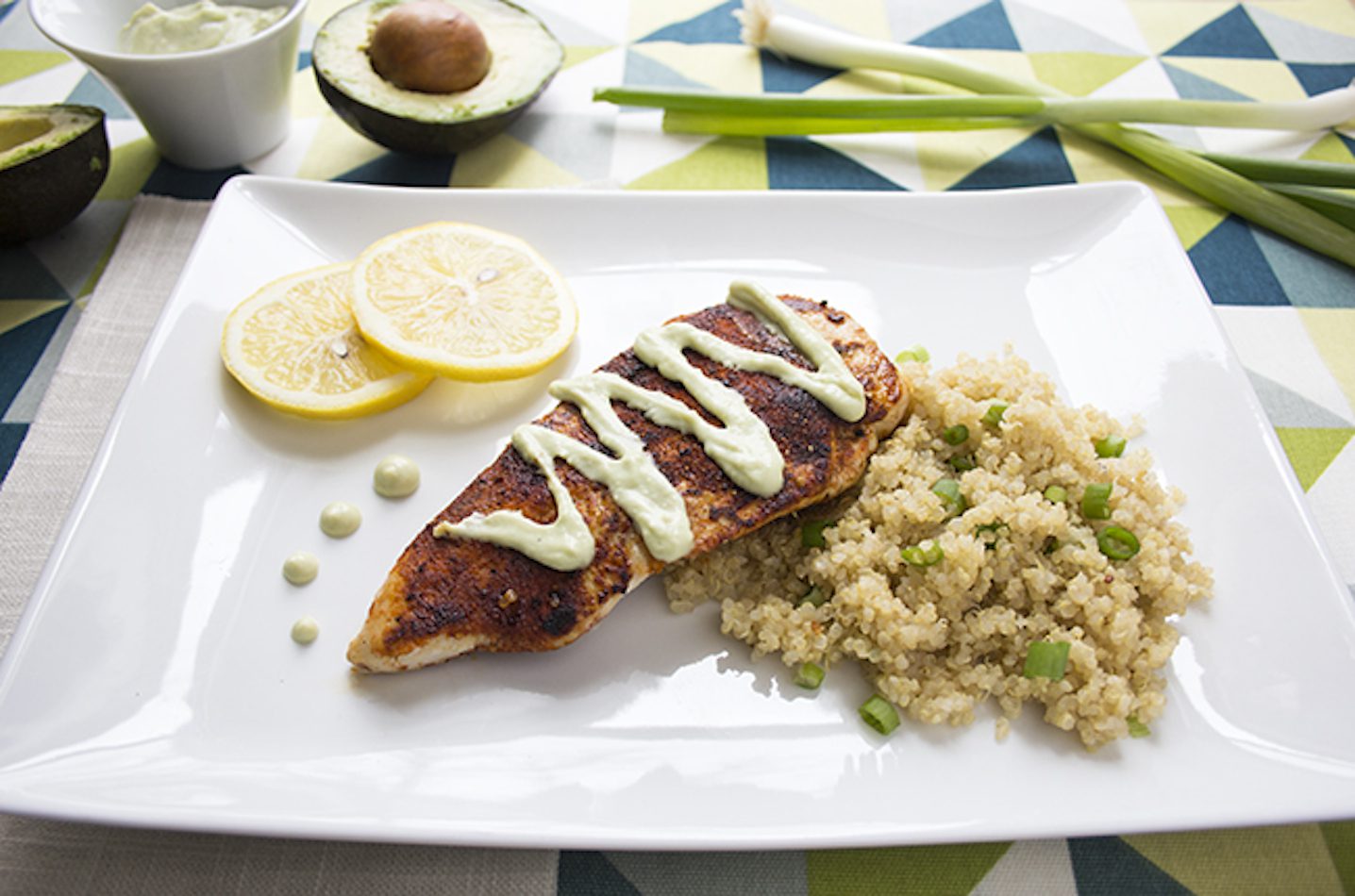 Blackened chicken with avocado cream sauce displayed on a white plate alongside rice sitting on a colorful tablecloth