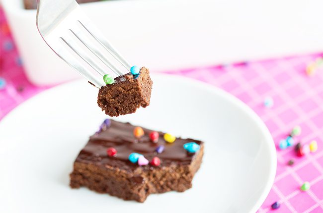 A slice of cosmic brownie on a white saucer with a bite on a fork