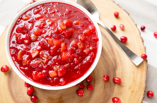 Overhead picture of white bowl filled with cranberry apple chutney sitting on a wooden surface