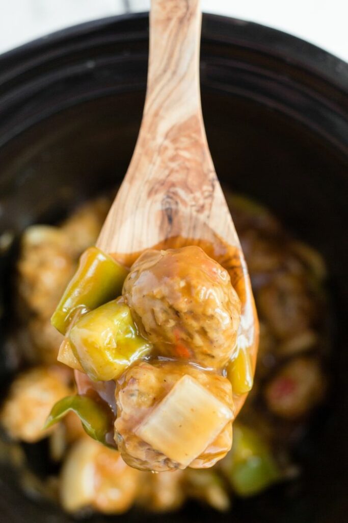 Up close picture of a wooden spoon over a slow cooker holding general tsos chicken