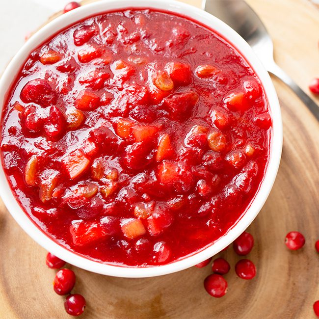 Up close picture of cranberry apple chutney relish in a large white bowl with a spoon to the side
