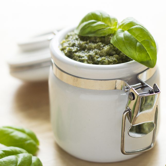 close up of basil pesto in a white jar