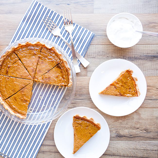 A healthy pumpkin pie sitting on a table with 2 slices sitting on white plates next to it