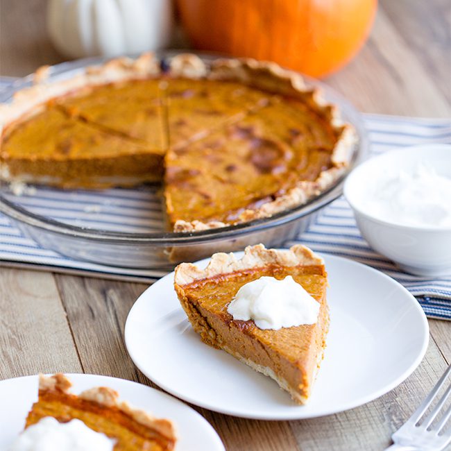 A sliced pumpkin pie with dollops of whipped cream on slices