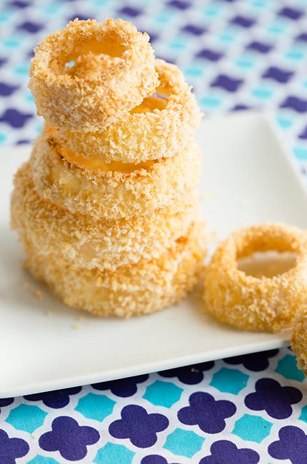 A large stack of onion rings ready to be eaten sitting on a white plate