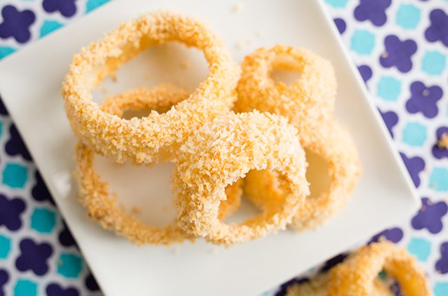 A white plate of baked onion rings sitting on a purple and teal patterned napkin