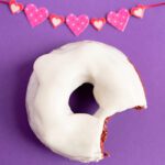 A red velvet donut on purple background with pink and white garland in background