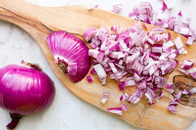 Chopped red onions on a small cutting board that is laying on a white surface