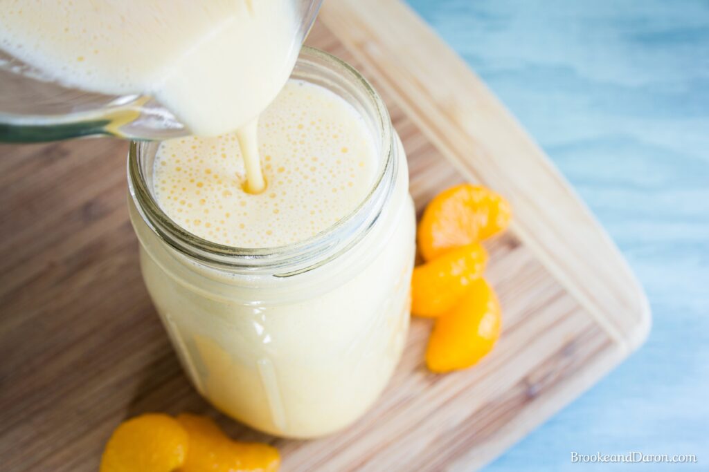 Pouring orange banana smoothie into mason jar