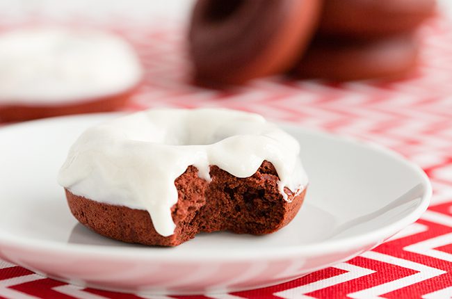 Red Velvet Donuts on white plate sitting on red and white chevron napkin with bite taken out