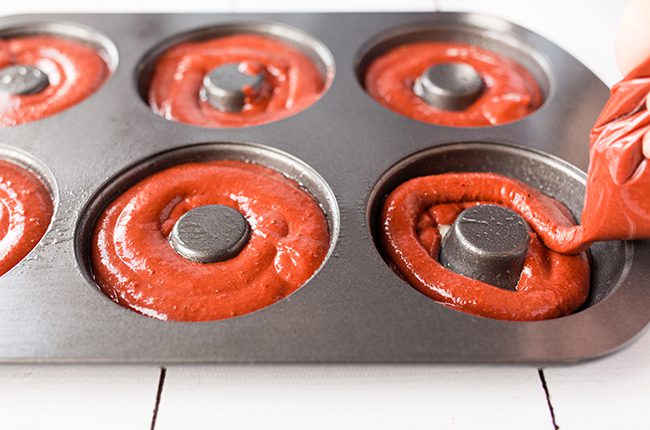 Pouring red velvet donuts batter into donut baking tin