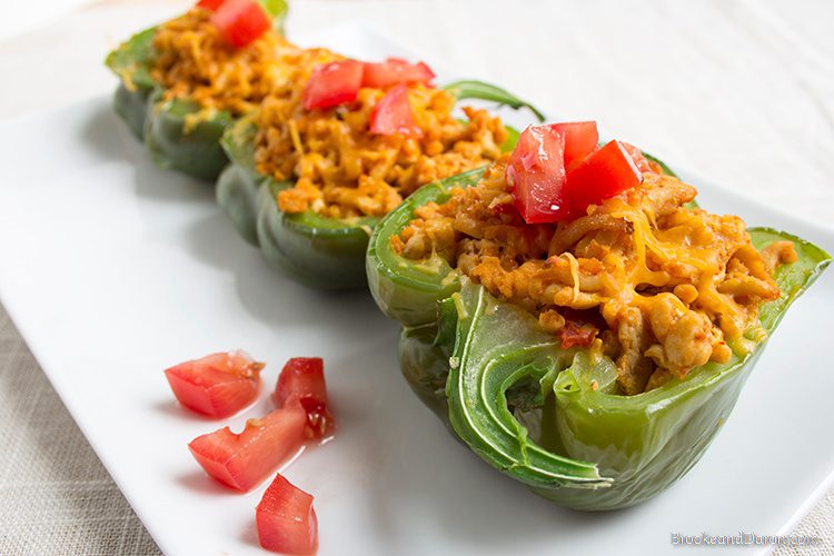 Three stuffed peppers on white plate with tomato