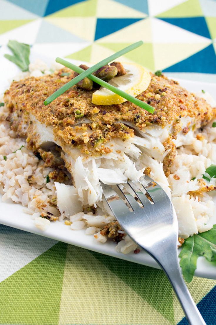 A fork taking a bite out of halibut on a white plate