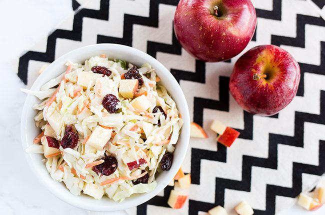 Overhead picture of apple coleslaw sitting on black and white napkin with apples beside it