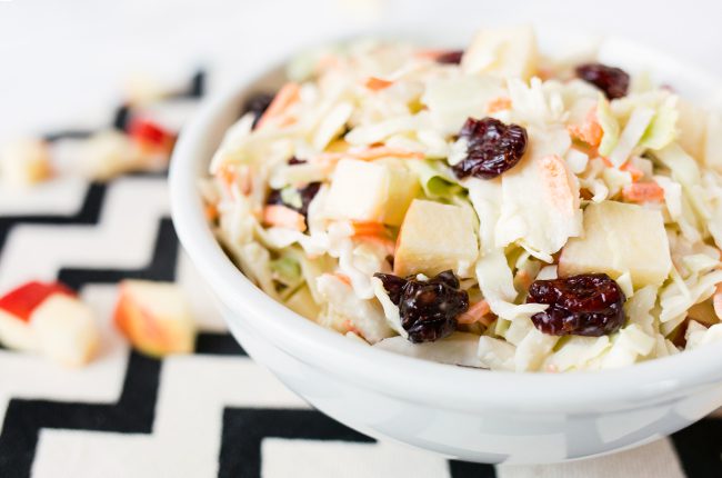 A picture of a white bowl filled with cranberry apple coleslaw sitting on a black and white napkin