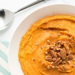 Overhead picture of white bowl of mashed sweet potatoes topped with pecans