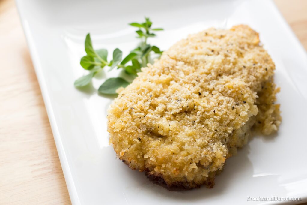 Parmesan pork chop on white plate with parsley