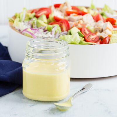 honey mustard dressing in mason jar with spoon and salad in bowl