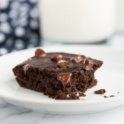 vertical image of black bean brownie on a plate with milk in background