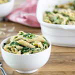 spinach pasta in a white bowl sitting in front of large white baking dish