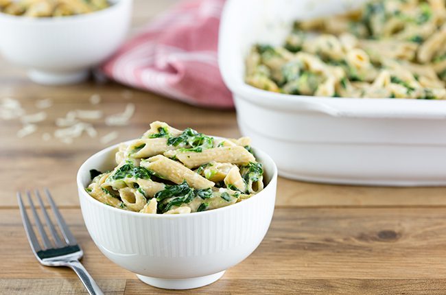 spinach pasta in a white bowl sitting in front of large white baking dish