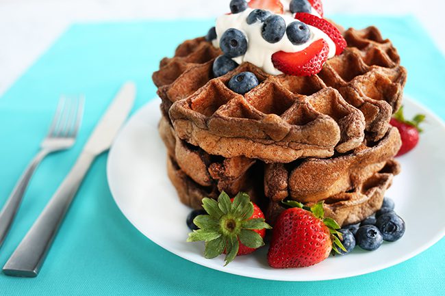 A stack of chocolate protein waffles on a white plate sitting on teal cloth