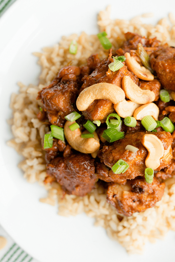 Slow Cooker Cashew Chicken on a white plate topped with cashews and green onions