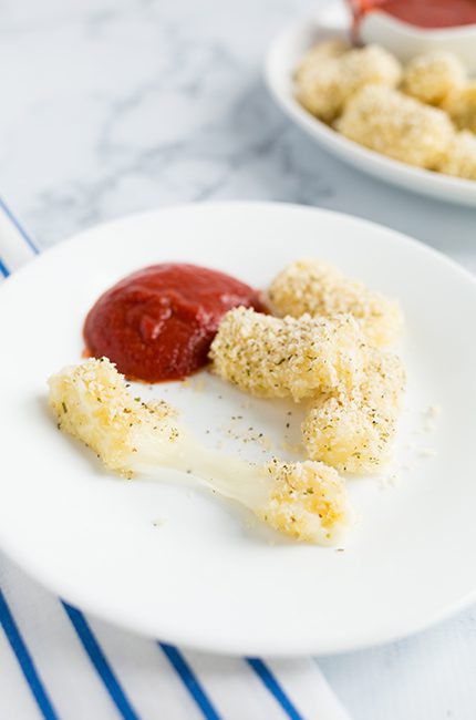 Mozzarella sticks sitting on a white plate being served with marinara sauce