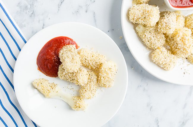 Baked healthy mozzarella sticks sitting on a white plate with marinara sauce