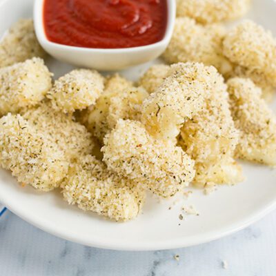 An up close picture of a white plate filled with baked mozzarella bites served with cup of marinara sauce