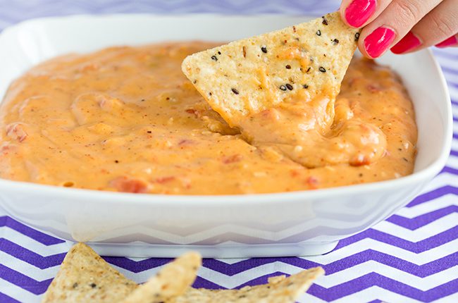 A large white bowl of queso dip sitting on a blue and white chevron cloth