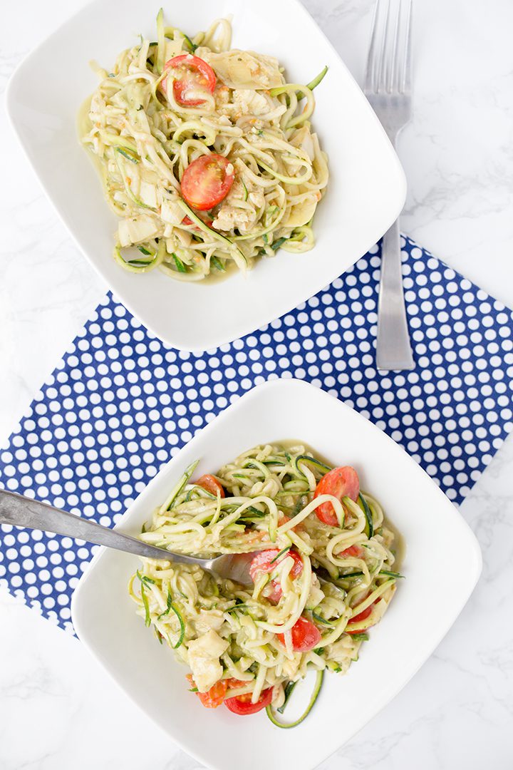 Two bowls of creamy avocado pasta with zoodles sitting on a white table with blue and white cloth