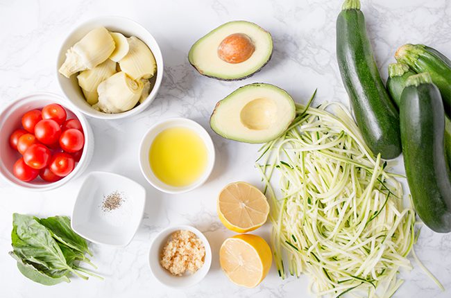 Ingredients for avocado pasta with zoodles laying on a white surface