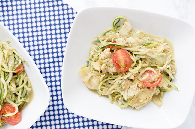 Creamy Avocado pasta made with zoodles and cherry tomatoes sitting in a white bowl on top of a blue checked cloth