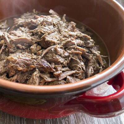 A red bowl full of prepared barbacoa recipe to use in burrito bowls