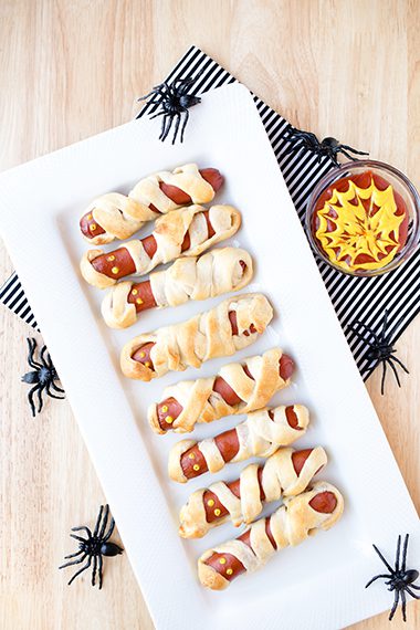 Long white platter of mummy hot dogs sitting on blue napkin