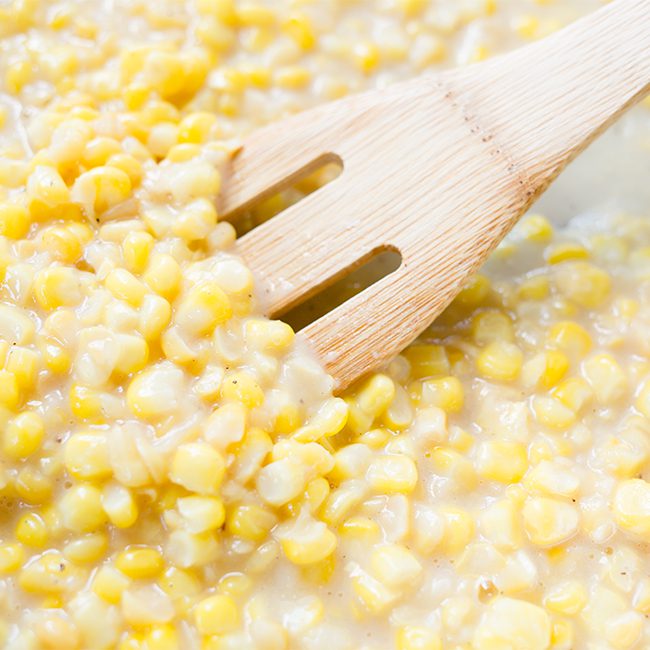 Up close image of homemade cream corn being stirred with wooden spoon