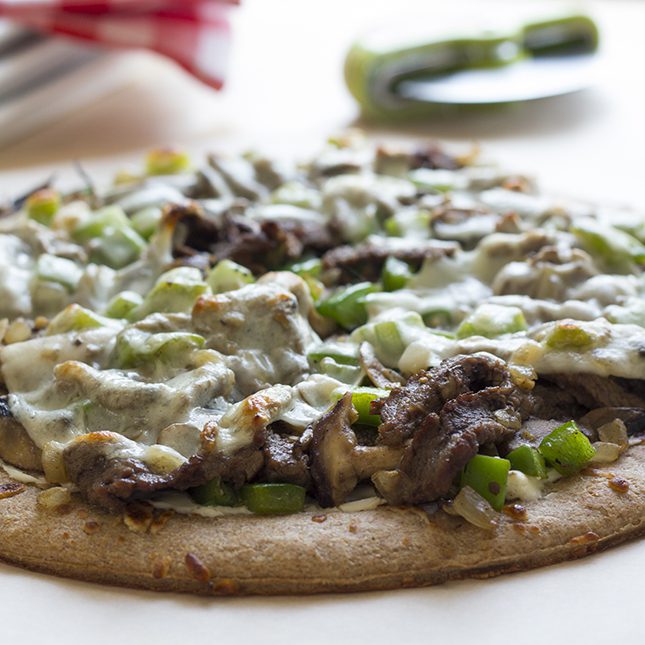 A close up image of a baked philly cheesesteak pizza