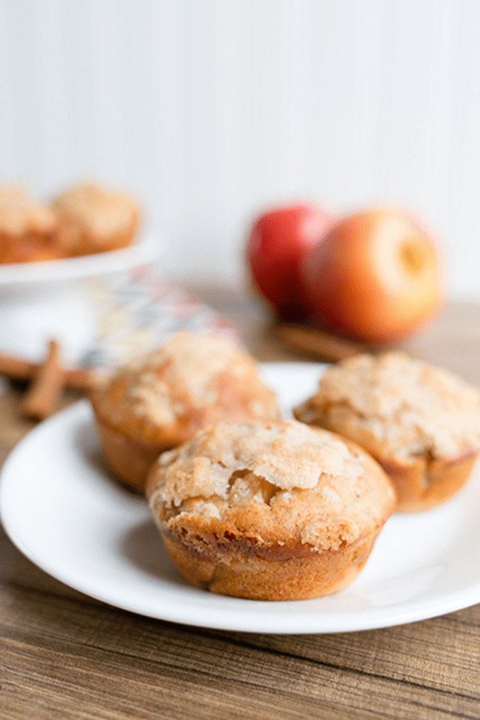 A white plate of apple cinnamon muffins sitting on a wooden table