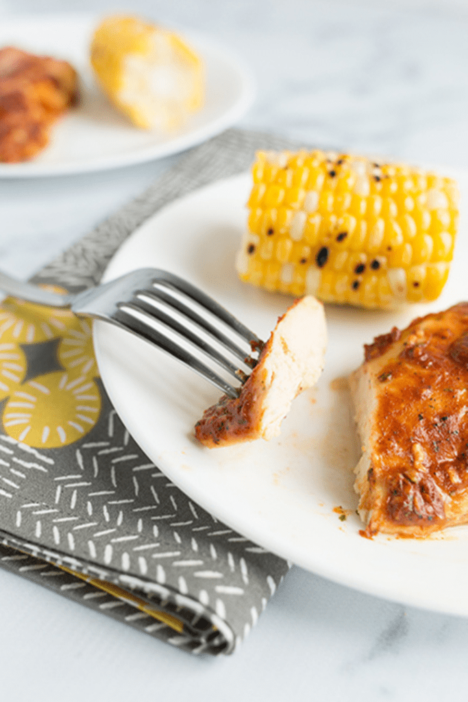 Baked chicken breast on white plate sitting on gray and yellow napkin