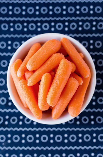 Overhead picture of white bowl of glazed carrots sitting on a blue and white cloth