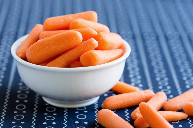 A white bowl of candied carrots sitting on a blue and white cloth
