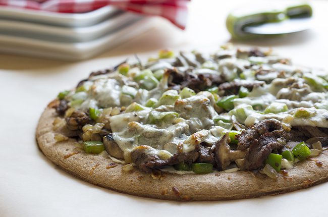 Cheesesteak pizza baked and ready to slice on a pizza board