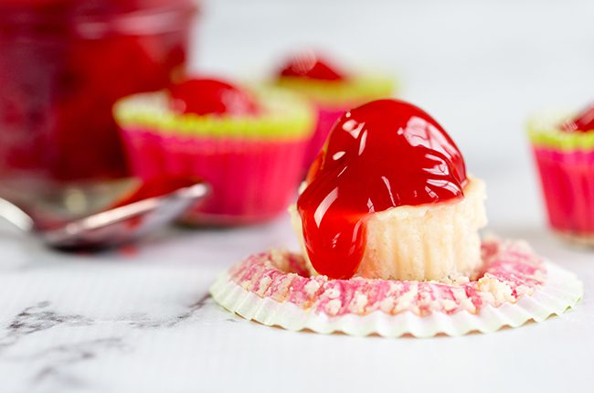 Mini cherry cheesecakes laying on a white marble surface topped with cherry topping