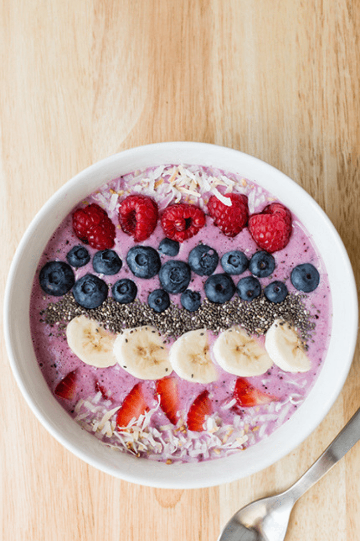 Overhead picture of a white bowl filled with a berry smoothie topped with fresh fruit and coconut