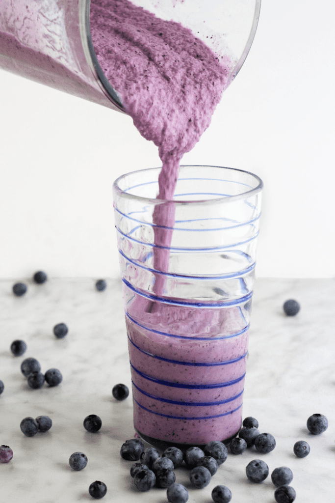Pouring blueberry smoothie into a tall glass