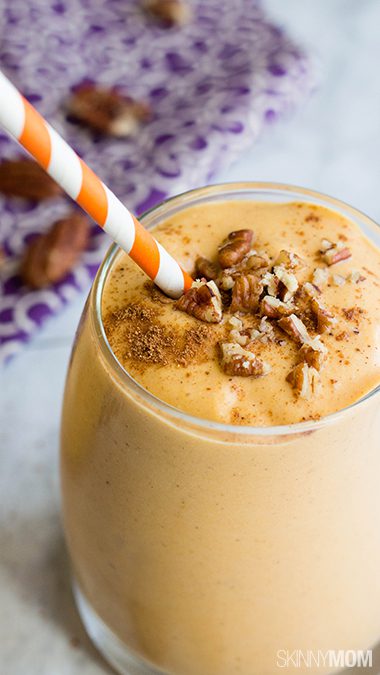 Single glass of pumpkin smoothie topped with chopped pecans, cinnamon and an orange and white paper straw